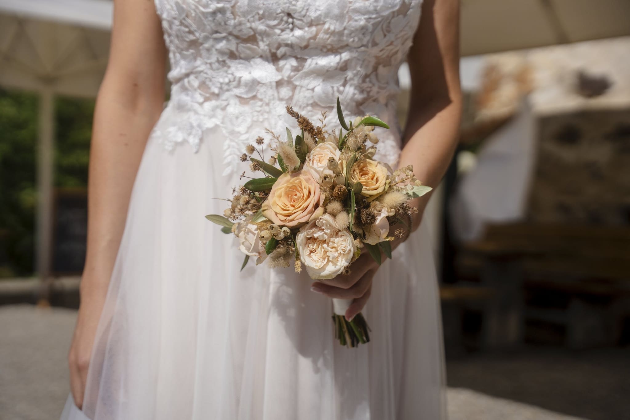 Braut im Spitzenkleid mit einem Strauss aus Rosen in Pfirsich und Creme