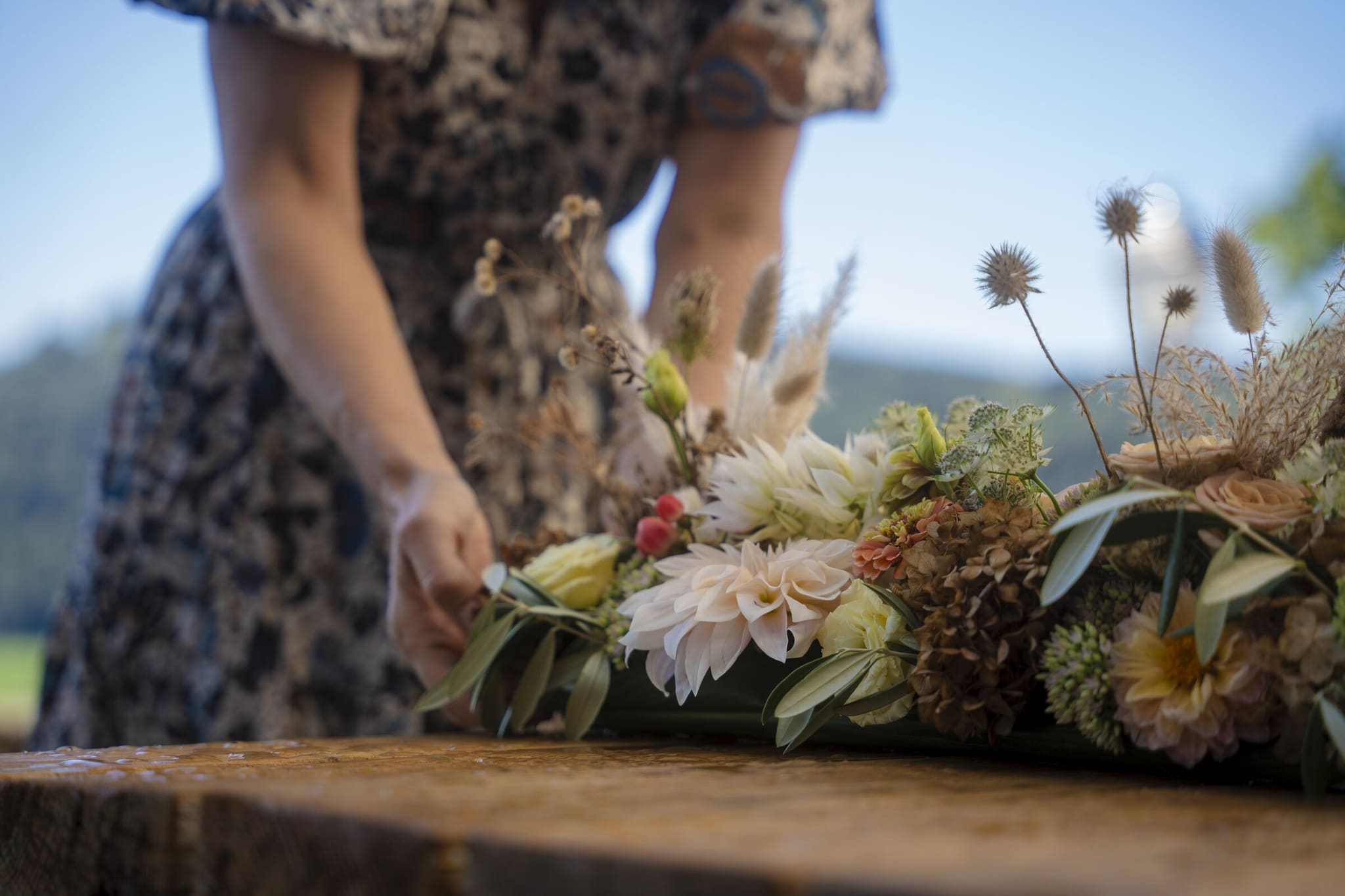 Floristin arrangiert eine Tischdekoration mit Dahlien und Disteln im Freien