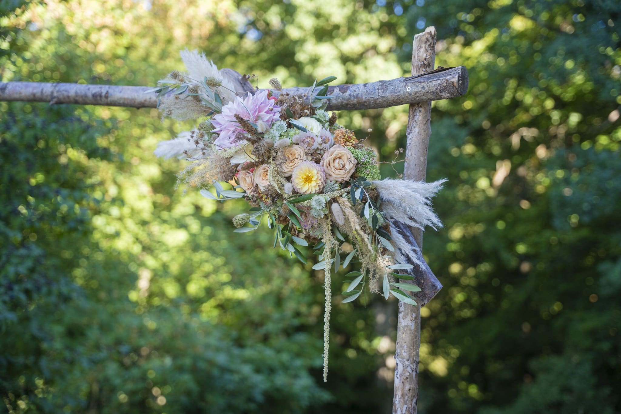 Blumengesteck mit Rosen und Pampasgras an einem Traubogen aus Holz